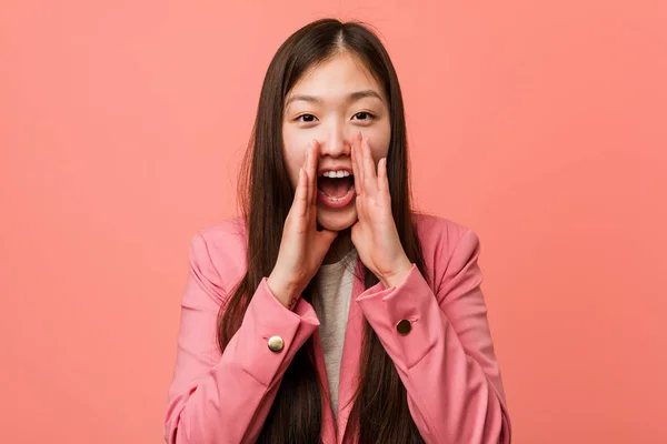 Young business chinese woman wearing pink suit shouting excited to front.