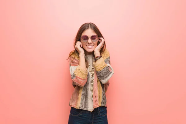 Young hippie woman on pink background covering ears with hands