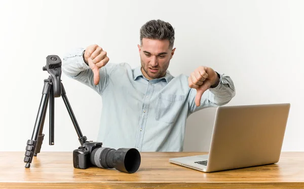 Young handsome photography teacher showing thumb down and expressing dislike.