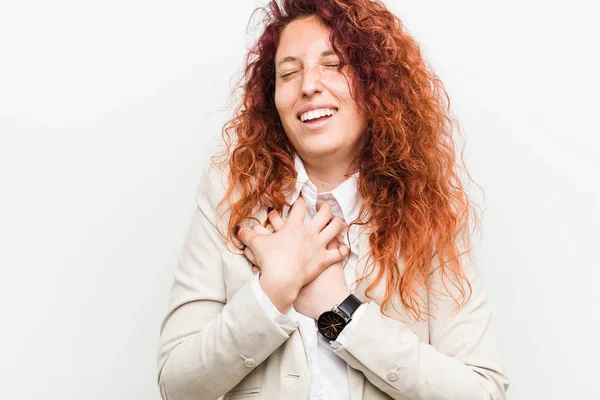 Young natural redhead business woman isolated against white background laughing keeping hands on heart, concept of happiness.