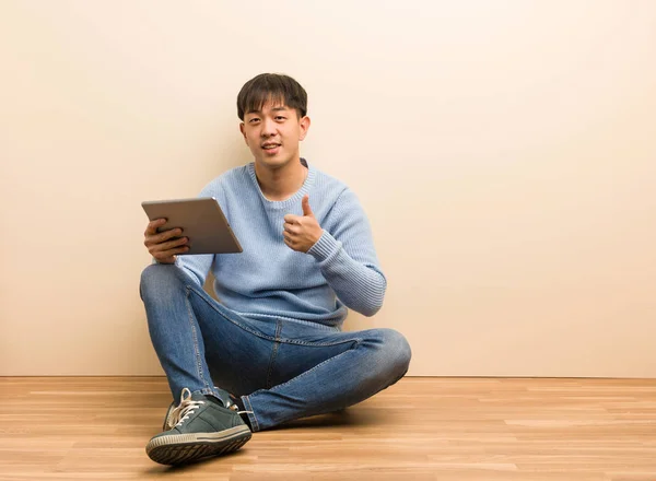 Young chinese man sitting using his tablet smiling and raising thumb up