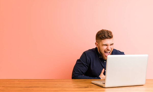 Молодой человек, работающий со своим ноутбуком, счастливо смеется и весело держит руки на животе.
.