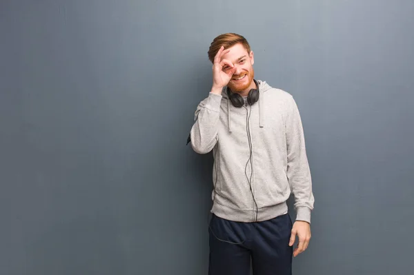 Young fitness redhead man confident doing ok gesture on eye