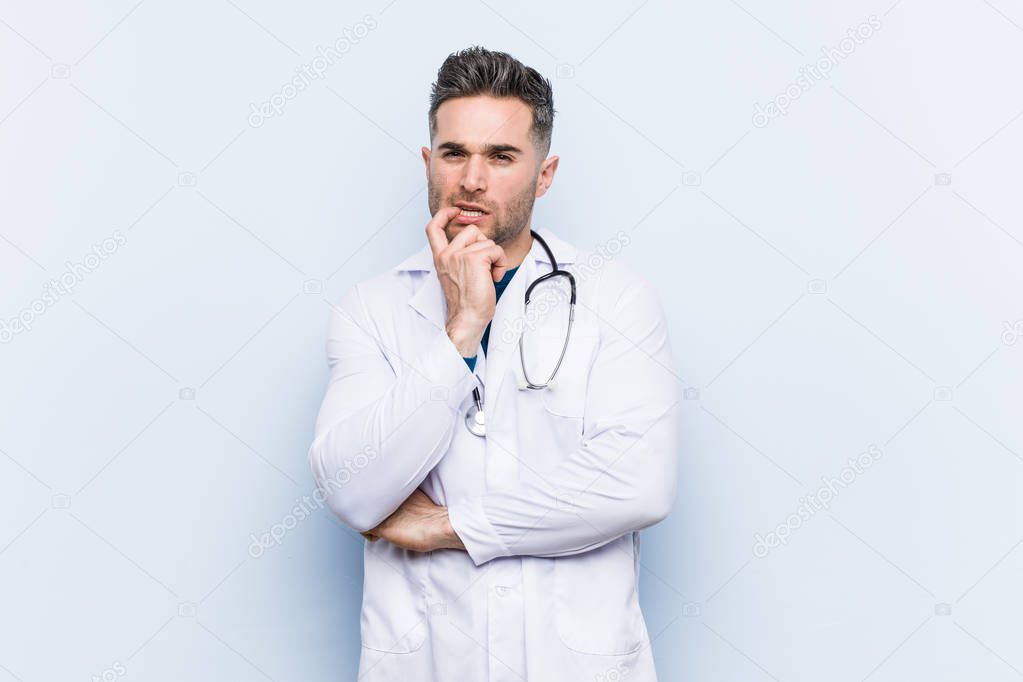 Young handsome doctor man relaxed thinking about something looking at a copy space.
