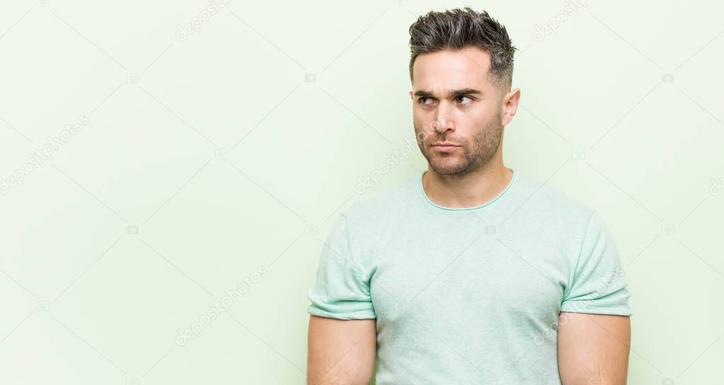 Young handsome man against a green background confused, feels doubtful and unsure.