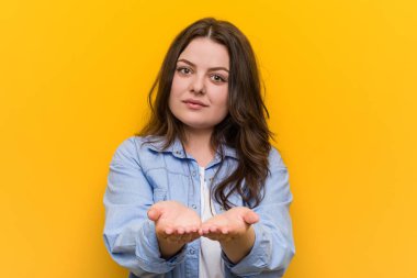 Young curvy plus size woman holding something with palms, offering to camera.