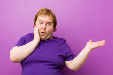 Genç otantik kızıl saçlı şişman adam bir avuç üzerinde kopya alanı tutar, yanak üzerinde el tutmak. Şaşırmış ve memnun.