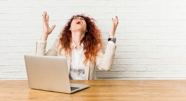 Genç kızıl saçlı kıvırcık kadın dizüstü bilgisayarıyla gökyüzüne bağırıyor, yukarı bakıyor, hayal kırıklığına uğramış..