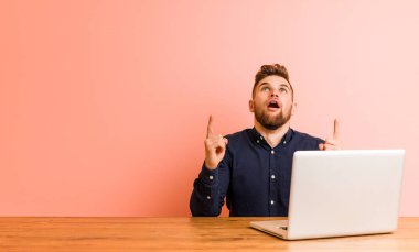 Dizüstü bilgisayarıyla çalışan genç adam ağzı açık bir şekilde üst tarafı işaret ediyor..