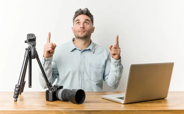 Young handsome photography teacher pointing upside with opened mouth.