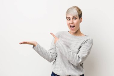 Beyaz arka planda izole edilmiş beyaz saçlı genç bir kadın palmiye ağacında bir kopya alanı tutarken heyecanlanıyor..