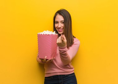 Genç, tatlı bir kadın elinde patlamış mısır kovası tutuyor ve gelmesi için davet ediyor