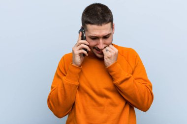 Kafkasyalı genç bir adam elinde telefonla tırnak yiyor, gergin ve çok endişeli..