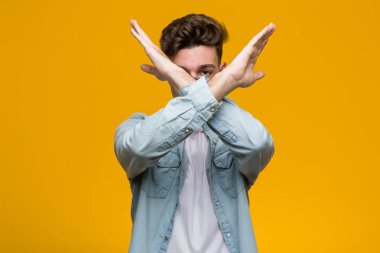 Kot gömlek giyen genç yakışıklı bir öğrenci iki kolu çapraz tutuyor, inkar kavramı..