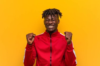 Genç fitness zencisi yumruğunu kaldırıyor, mutlu ve başarılı hissediyor. Zafer konsepti.