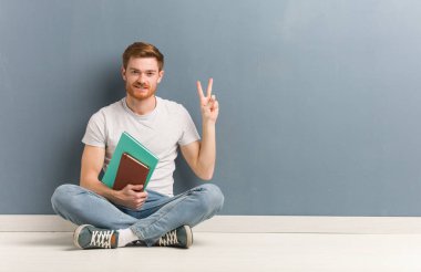 Genç kızıl saçlı öğrenci iki numarayı göstererek yerde oturuyor. Elinde kitaplar var..
