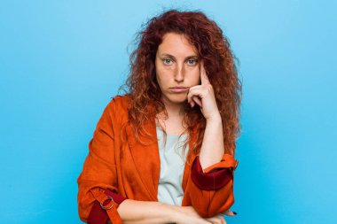 Genç kızıl saçlı zarif bir kadın şakağı parmağıyla işaret ediyor, düşünüyor, bir göreve odaklanıyor..