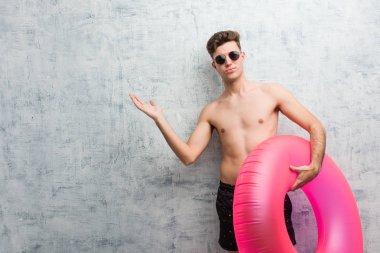 Elinde pembe şişme bir donut tutan genç adam mayo giyiyor ve sorgulama sırasında omuzlarını silkiyor..