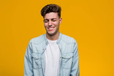 Kot gömlek giyen genç yakışıklı öğrenci gülüyor ve gözlerini kapatıyor, rahatlamış ve mutlu hissediyor..