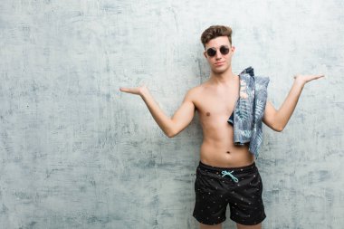 Mayo giyen genç beyaz adam kollarıyla ölçek yapıyor, mutlu ve kendinden emin hissediyor..