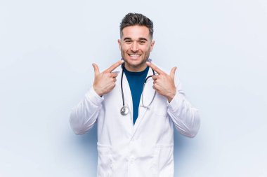 Genç, yakışıklı doktor gülümsüyor, parmaklarını ağzına doğrultuyor..