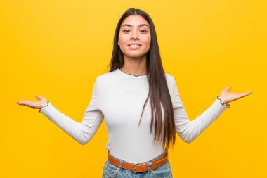 Sarı arka planda genç ve güzel bir Arap kadın kollarıyla ölçeği yapıyor, mutlu ve kendinden emin hissediyor..