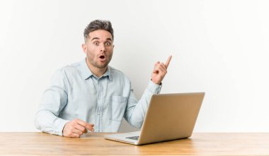 Laptopuyla çalışan yakışıklı genç adam yan tarafı işaret ediyor.