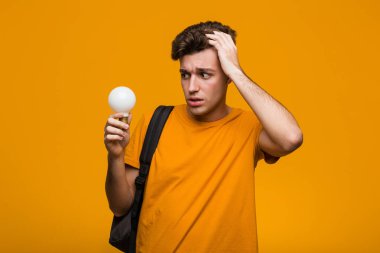 Elinde ampul tutan genç bir öğrenci. Neşeli gülümsemeler ön tarafı işaret ediyor..