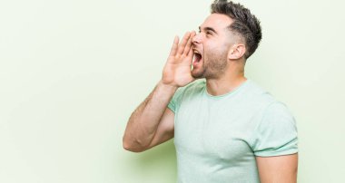 Yeşil arka planda genç yakışıklı bir adam bağırıyor ve avuç içini açık tutuyor..