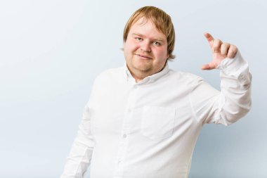 Genç otantik kızıl saçlı şişman adam işaret parmaklarıyla küçük bir şey tutuyor, gülümsüyor ve kendinden emin..