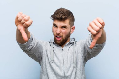 Genç yakışıklı fitness adamı baş parmağını aşağı gösteriyor ve hoşlanmadığını ifade ediyor..