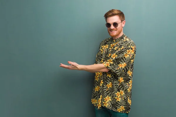 Young redhead man wearing exotic summer clothes holding something with hands