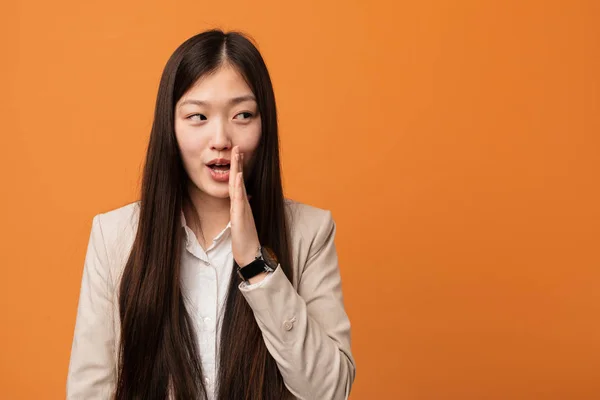 Young business chinese woman is saying a secret hot braking news and looking aside