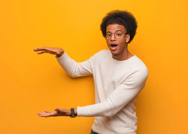 Young African American Man Orange Wall Holding Something Very Surprised — Stock Photo, Image