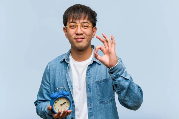 Молодой Китаец Держит Руках Будильник Веселый Уверенный Себе Жест Порядке — стоковое фото