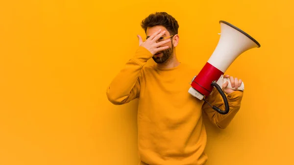 Young man holding a megaphone embarrassed and laughing at the same time