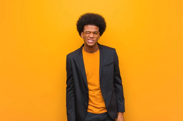 Young business african american man over an orange wall winking, funny, friendly and carefree gesture
