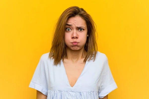 Young pretty young woman blows cheeks, has tired expression. Facial expression concept.