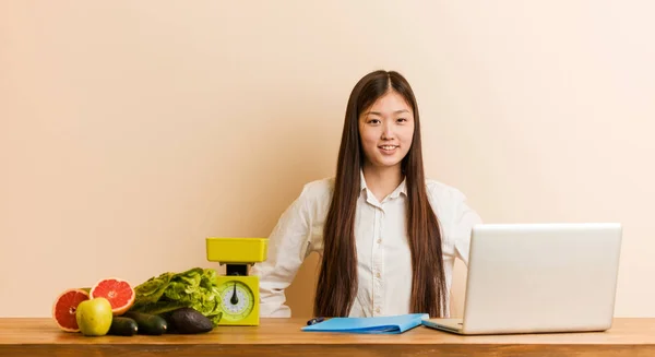 Young nutritionist chinese woman working with her laptop confident keeping hands on him hips.