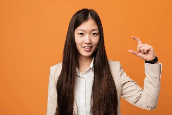Young business chinese woman holding something little with forefingers, smiling and confident.