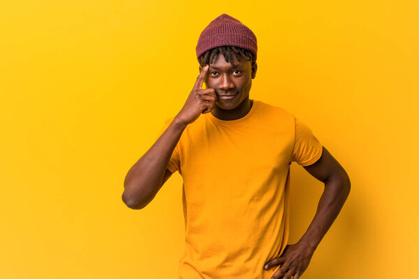 Young black man wearing rastas over yellow background pointing temple with finger, thinking, focused on a task.