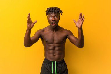 Genç siyah adam gömleksiz giyen mayo hoş bir sürpriz alma, heyecanlı ve eller yetiştirme.