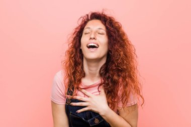 Bir kot dungaree giyen genç güzel kızıl saçlı kadın yüksek sesle göğüs üzerinde el tutmak dışarı gülüyor.