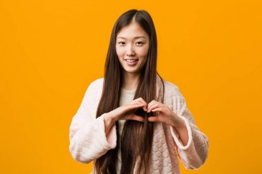 Pijama Genç Çinli kadın gülümseyen ve ona elleri ile kalp şekli gösteren.