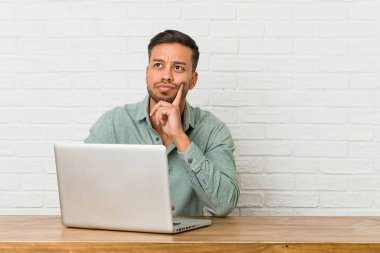 Genç Filipino adam oturan onun laptop ile yan şüpheli ve şüpheci ifade bakıyor.