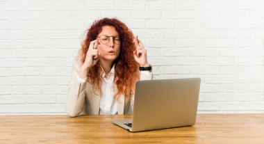 Genç kızıl saçlı kıvırcık kadın şans için onun dizüstü geçiş parmakları ile çalışıyor