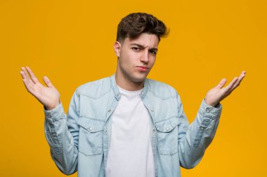 Genç yakışıklı öğrenci bir kot gömlek giyen şüphe ve sorgulama jest onu omuzsilke.