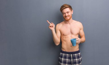 Genç gömleksiz kızıl adam parmakla yan gösteren. Elinde bir kahve bardağı tutuyor..