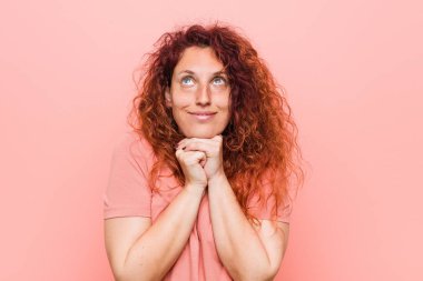 Genç doğal ve otantik kızıl saçlı kadın çene altında ellerini tutar, bir kenara mutlu bakıyor.