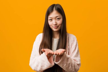 Pijama Genç Çinli kadın avuç içi ile bir şey tutan, kamera sunan.